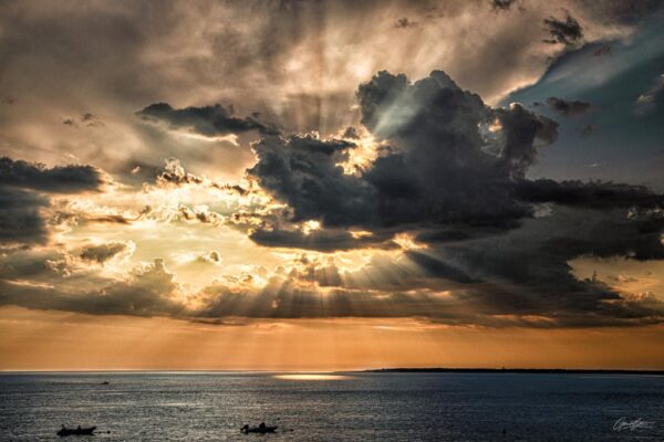 Vue du Cap Ferret à l'horizon, dominé par un ciel spectaculaire où un gros nuage laisse passer des rayons de soleil éclatants, illuminant le paysage