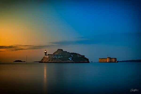Sous les teintes dorées d’un coucher de soleil, l’ile Louet et le château du Taureau se dressent majestueusement en baie de Morlaix. L’île, surmontée de son phare emblématique, semble flotter sur les eaux calmes, tandis que le château, vestige historique, veille sur l’horizon. Ce tableau naturel et intemporel capture la sérénité et la magie de ce lieu unique, où la lumière du crépuscule sublime chaque détail du paysage