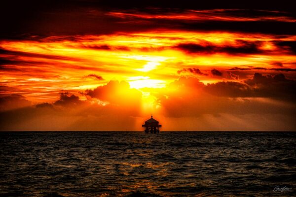Coucher de soleil avec des rayons traversant les nuages, illuminant le phare du bout du monde